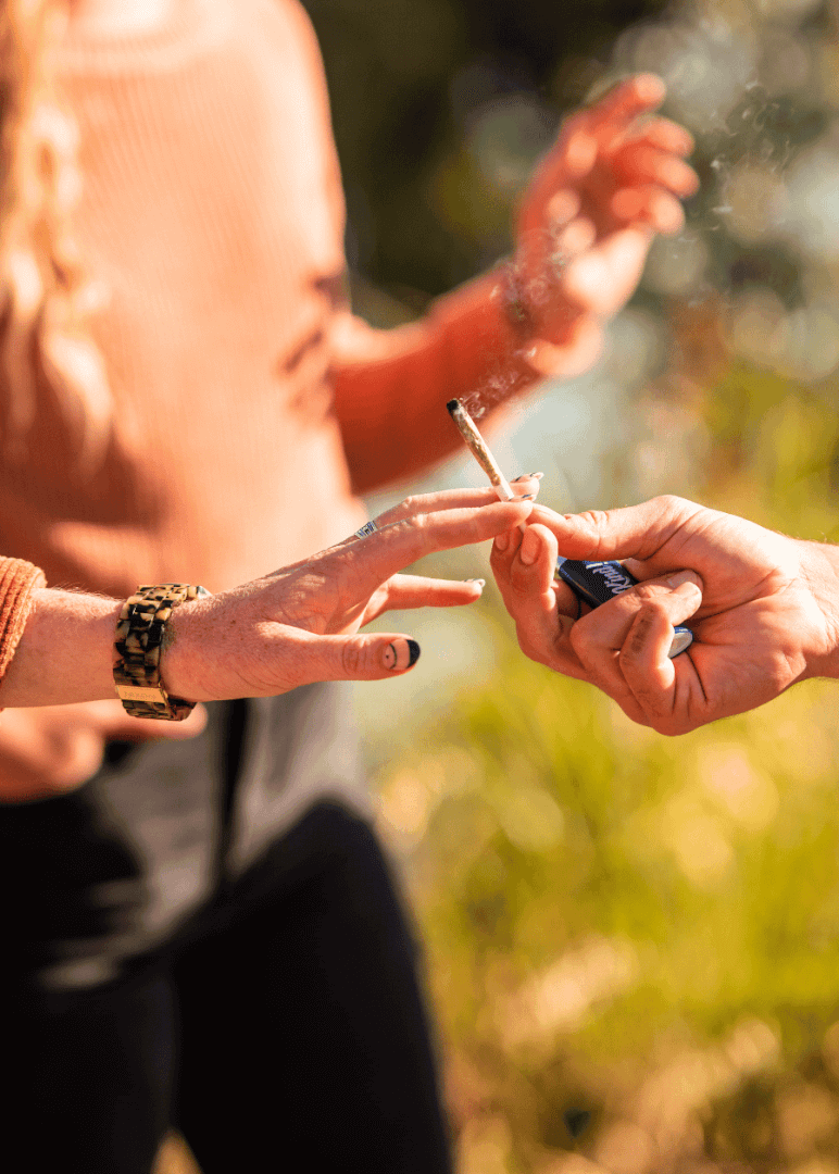 Two people pass a lit infused pre roll from Highway Cannabis Dispensary in Marina Del Rey back and forth between each other out in nature.
